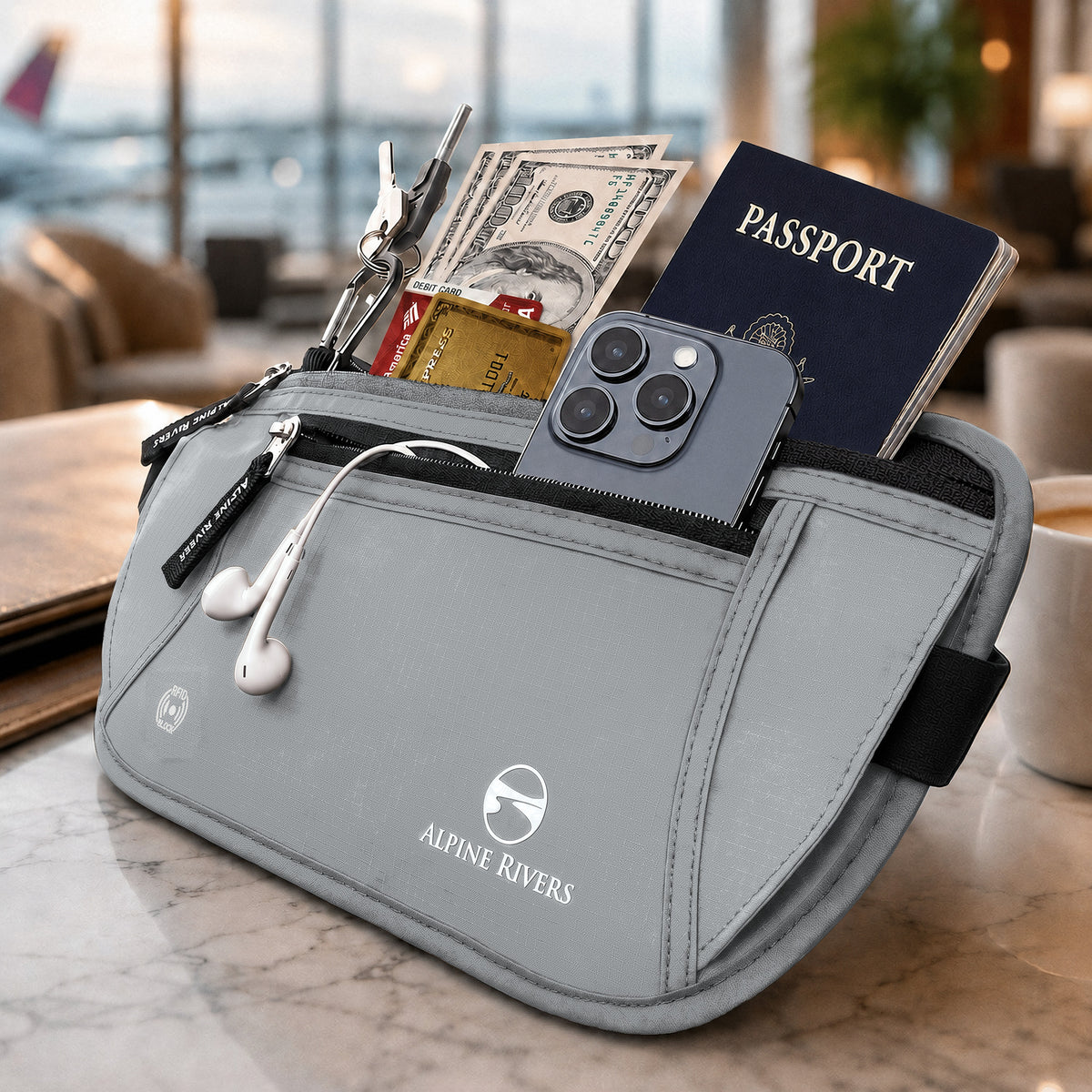 Alpine Rivers RFID blocking money belt in Graphite Gray holding a passport, cash, cards, phone, earphones and keys on a marble table in an airport lounge